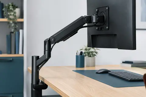 Bras d’écran articulé noir fixé à un bureau, avec moniteur et câbles guidés le long du support.